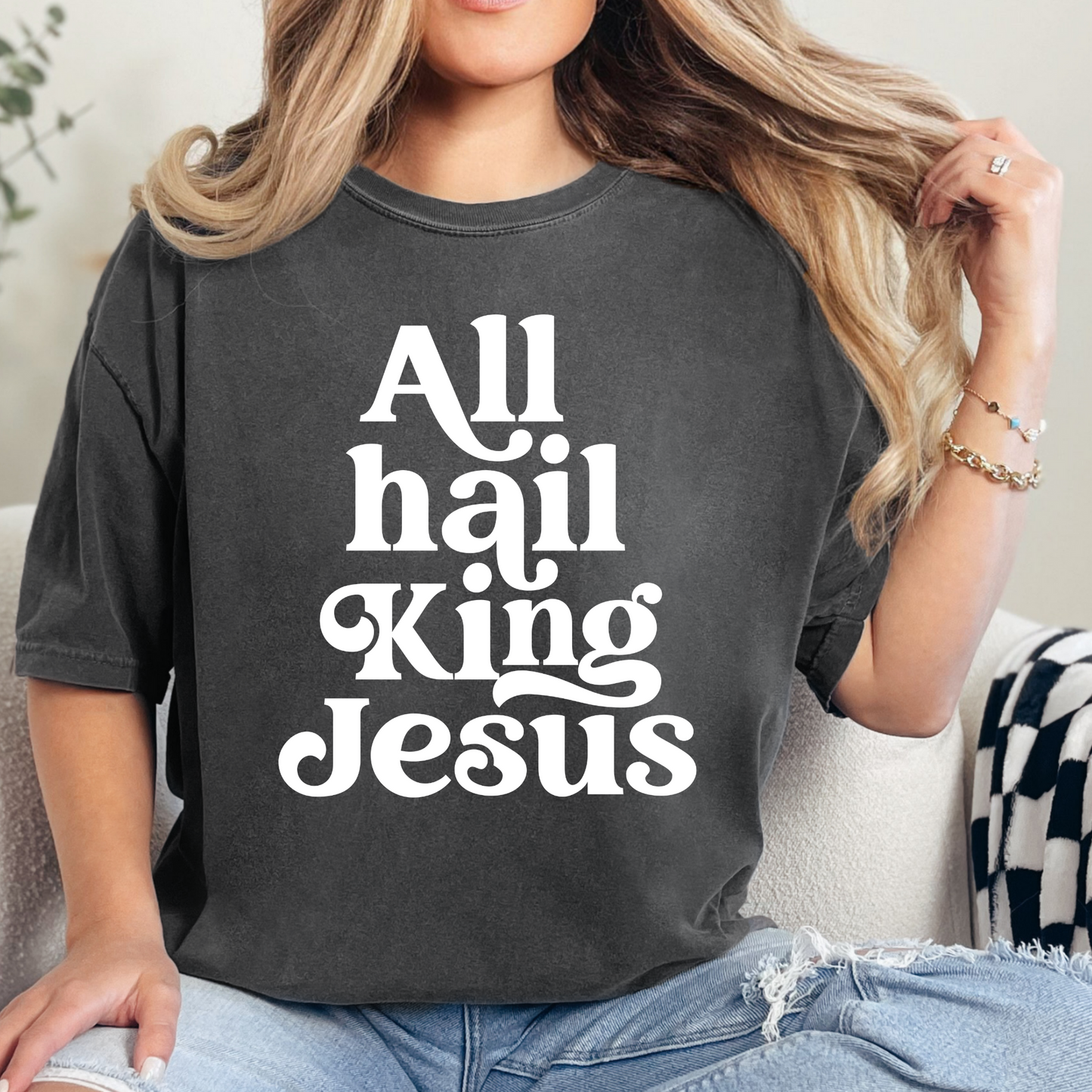 Unisex dark grey colored T-shirt with a retro text that says "All hail King Jesus". The design is direct to garment (DTG) printed on a pepper-colored Comfort Colors T-shirt, and is available in sizes S-3XL. The t-shirt is perfect for church-goers or as an inspirational gift.