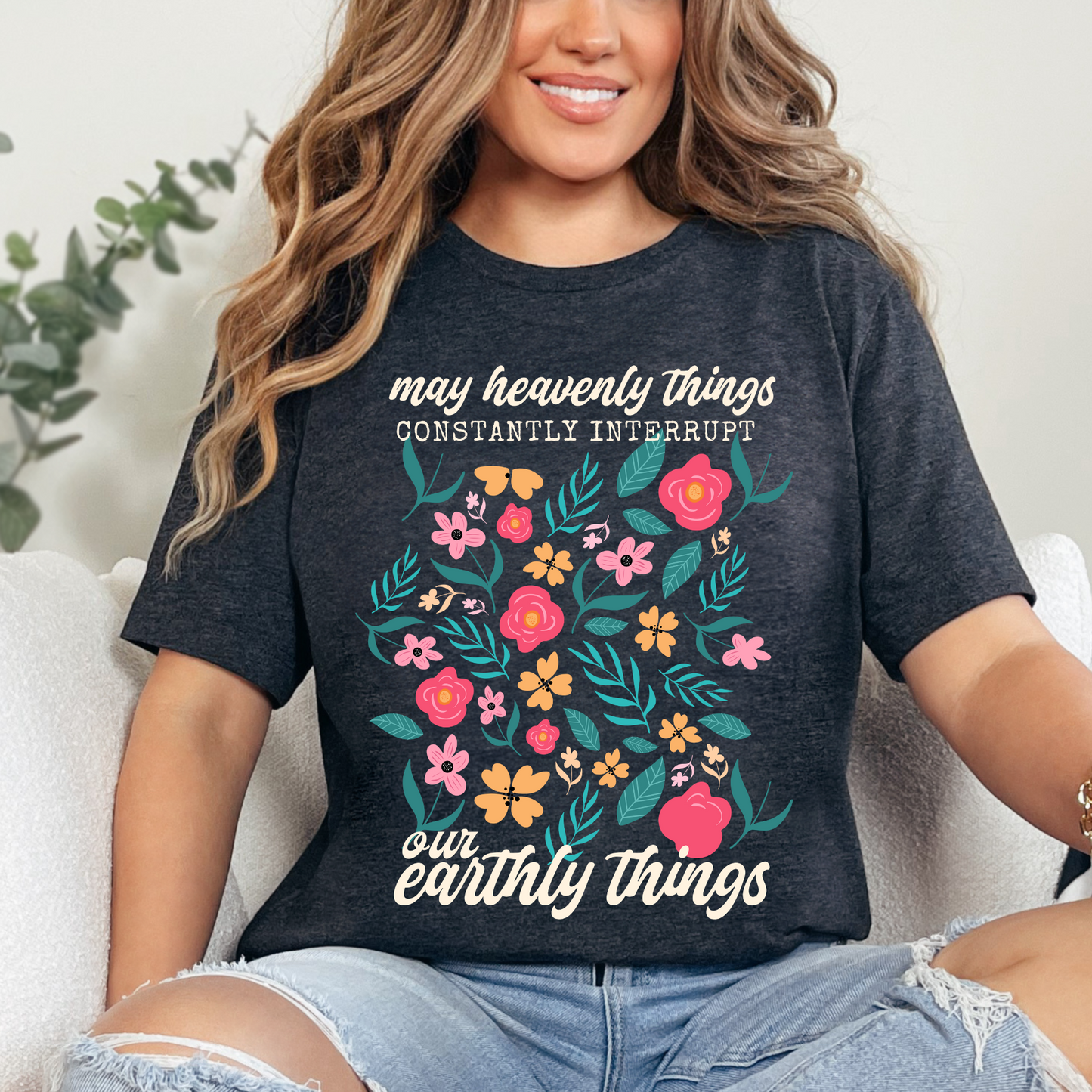 Christian T-shirt with a bright and colorful floral design that says "May heavenly things constantly interrupt our earthly things". The design is direct to garment (DTG) printed on a dark heather grey colored Bella + Canvas  brand t-shirt and available in sizes S-3XL.