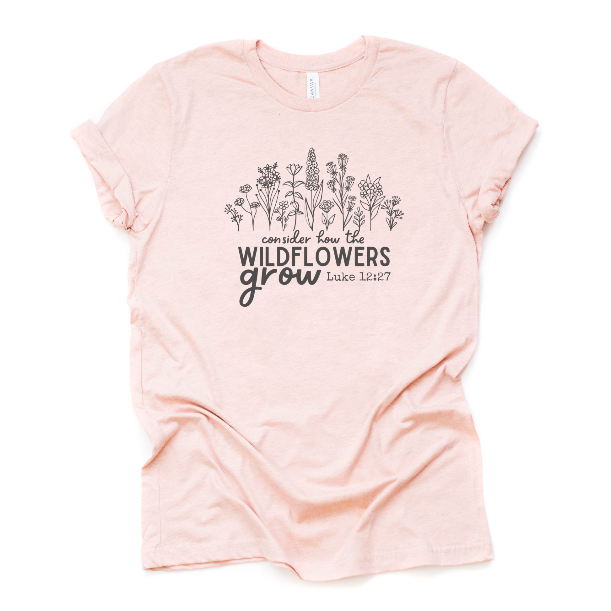 Christian T-shirt with wildflower illustration and text that says "Consider how the wildflowers grow", referencing the Luke 12:27 Bible verse. The design is direct to garment (DTG) printed on a heather prism peach colored Bella + Canvas  brand t-shirt and available in sizes S-3XL.